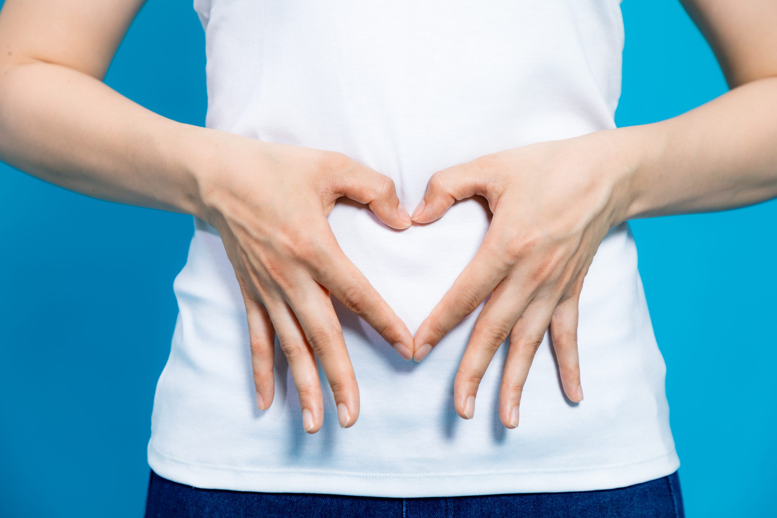 young woman who makes a heart shape by hands on her stomach. relaxation yoga auto soin jeûne nutrition Raphaël Perez
